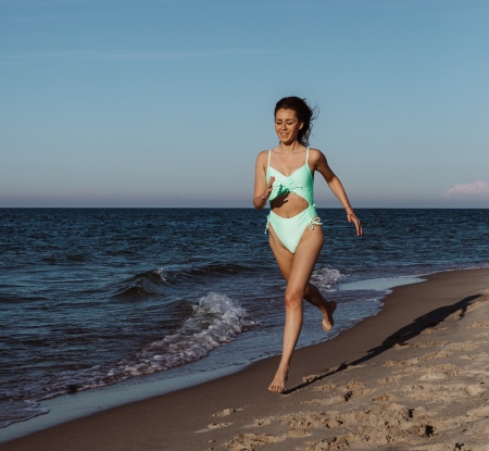 Bežiaca žena v plavkách Roxy na pláži pri západe slnka
